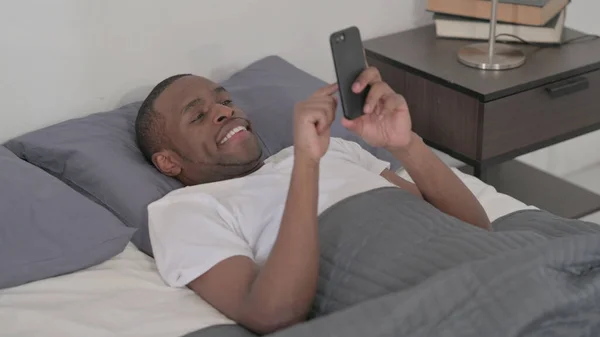 Young African Man Using Smartphone While Sleeping Bed Close — Fotografia de Stock