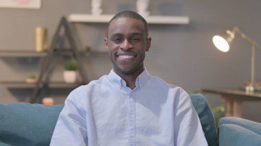 The Portrait of Young African Man Showing Yes Sign while Sitting on Sofa