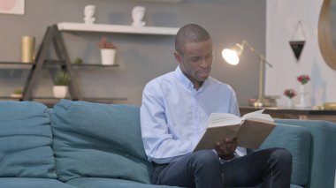 The Young African Man Reading Book while Sitting on Sofa