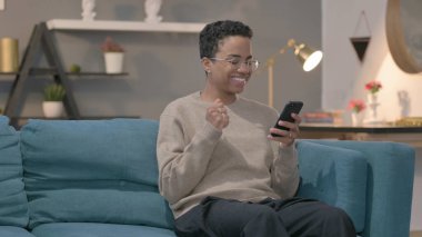 The African Woman Celebrating Success on Smartphone at home