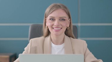 Ofiste dizüstü bilgisayar kullanırken kameraya gülümseyen Genç İş kadınının Kapanışı