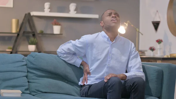 The Young African Man having Back Pain while Sitting on Sofa