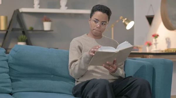 Young African Woman Thinking While Reading Book Sofa — 스톡 사진