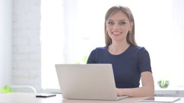 Dizüstü bilgisayar kullanırken Kameraya Gülümseyen Genç Kadın