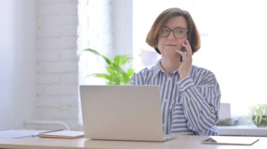 Laptop kullanırken telefonda konuşan yaşlı kadın.