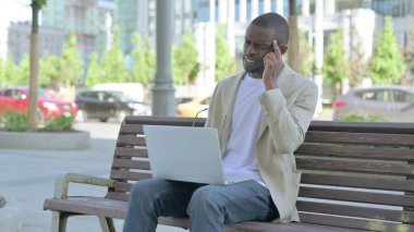 Baş ağrısı olan Afrikalı Amerikalı Adam Bench 'te otururken dizüstü bilgisayar kullanıyor.