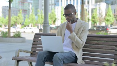 Bench 'te otururken dizüstü bilgisayar kullanan Afrikalı Amerikalı bir adam.