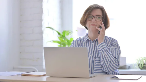 Vecchia Donna Che Parla Telefono Durante Utilizzo Del Computer Portatile — Foto Stock