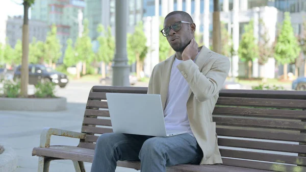 African American Man with Neck Pain Using Laptop while Sitting Outdoor on Bench