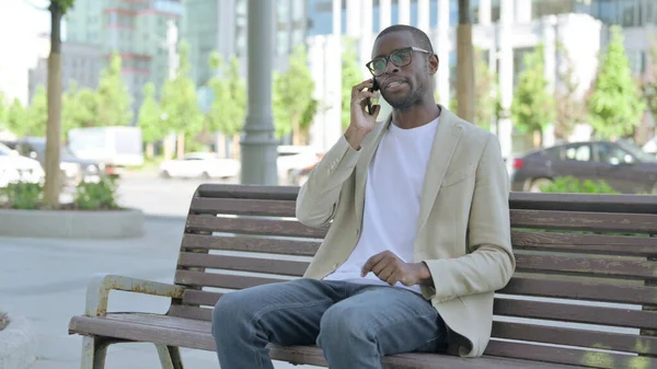 African American Man Talking on Phone while Sitting Outdoor on Bench