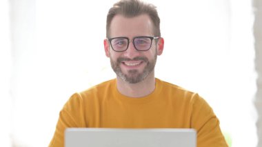 Bilgisayarlı orta yaşlı adam Kamerada gülümsüyor