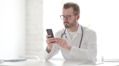 Klinikte akıllı telefon kullanan çekici orta yaşlı doktor.