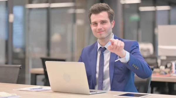 Middle Aged Businessman Pointing at Camera while using Laptop in Office