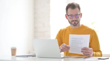 Middle Aged Man with Laptop Reading Documents in Office
