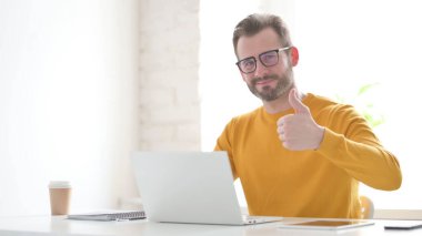 Ofiste dizüstü bilgisayar kullanırken Orta Yaşlı Adam İşaretini Gösteriyor