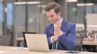 Ofiste dizüstü bilgisayar kullanırken bilek ağrısı çeken orta yaşlı bir iş adamı.