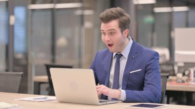 Ofiste dizüstü bilgisayar kullanırken Orta Yaşlı İşadamı Başarı Kutlaması