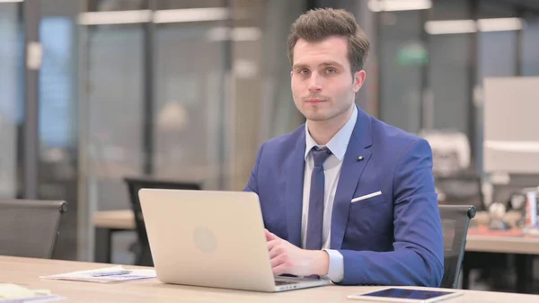 Middle Aged Businessman Shaking Head as No Sign while using Laptop in Office