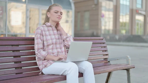 Casual Woman with Neck Pain Using Laptop while Sitting Outdoor on Bench