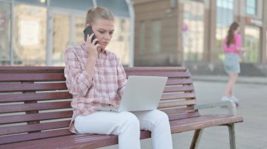Casual Woman Talking on Phone and using Laptop while Sitting Outdoor on Bench