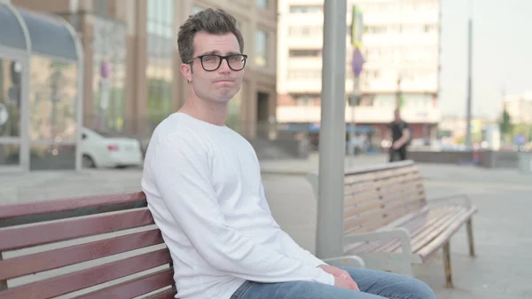 Rejecting Casual Man Shaking Head in Denial while Sitting on Bench