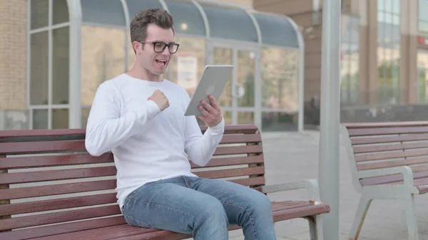 Casual Man Celebrating Online Win on Tablet while Sitting Outdoor on Bench