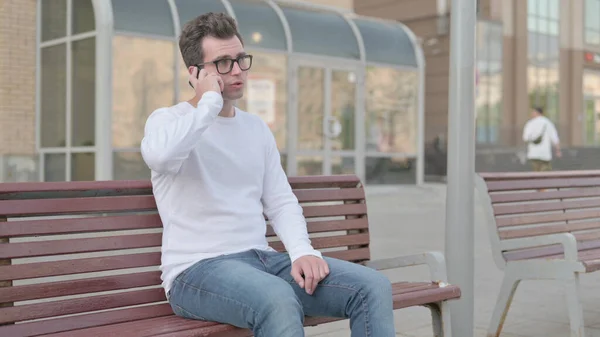 Casual Man Talking on Phone while Sitting Outdoor on Bench