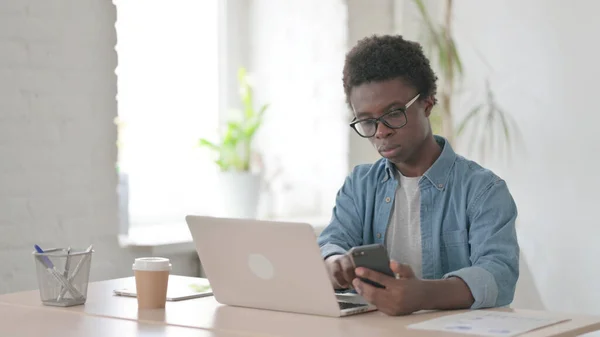 African Man Browsing Internet Smartphone While Using Laptop Office — Stockfoto