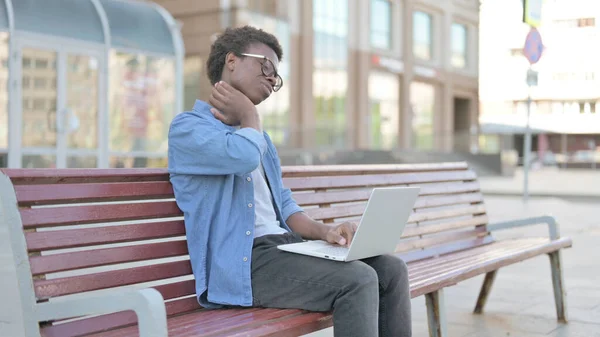 African Man with Neck Pain Using Laptop while Sitting Outdoor on Bench