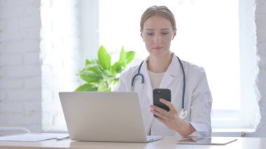 Klinikte dizüstü bilgisayar kullanırken Smartphone kullanan kadın doktor