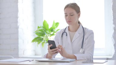 Klinikte otururken akıllı telefon kullanan kadın doktor.