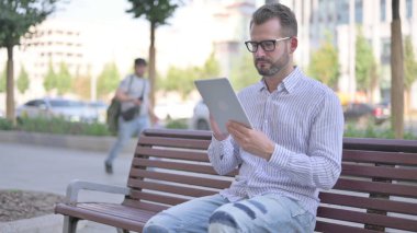 Adult Man using Tablet while Sitting Outdoor on Bench