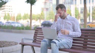 Adult Man with Headache Using Laptop while Sitting Outdoor on Bench