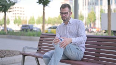Adult Man having Knee Pain while Sitting on Bench Outdoor