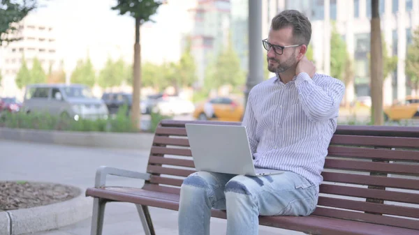 Adult Man with Neck Pain Using Laptop while Sitting Outdoor on Bench