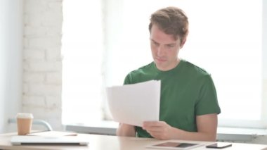 Ofiste otururken gelişigüzel genç adam belgeleri okuyor.