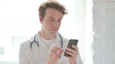 Male Doctor using Smartphone While sitting in Clinic