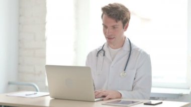 Male Doctor Talking on Video Call on Laptop in Clinic