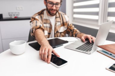 Tatmin olmuş bir adam iş arasında masadan bir cep telefonu alıyor.