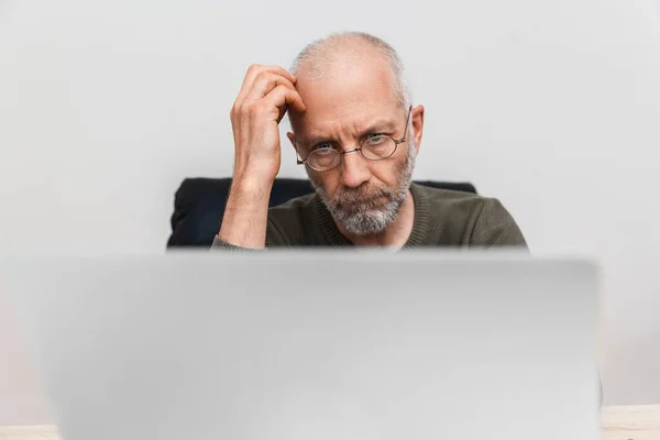 Elderly pensive man working on a laptop
