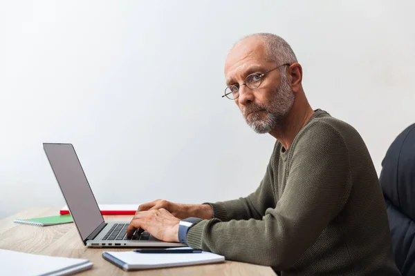 Äldre Man Som Arbetar Bärbar Dator Och Tittar Kameran Stockbild