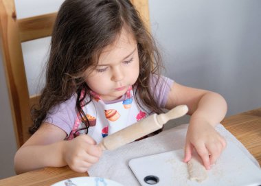 Genç kız mutfak masasında kostümlü şefmiş gibi rol yapıyor.