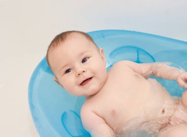 Küçük bebek mavi bir bebek küvetinde banyo yapıyor.