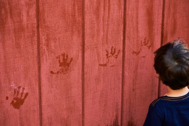 Küçük bir çocuk ıslak elleriyle çitin üzerinde el izi bırakıyor.