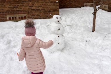 Pembe kışa uygun giyinmiş küçük kız bir kardan adama son rötuşları yapıyor.