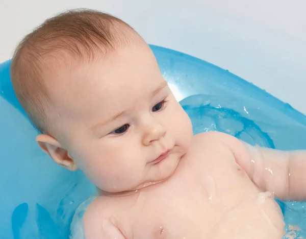 Küçük bebek mavi bir bebek küvetinde banyo yapıyor.