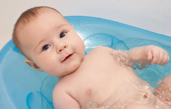 Küçük bebek mavi bir bebek küvetinde banyo yapıyor.