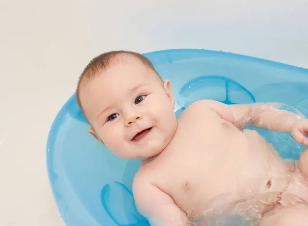 Küçük bebek mavi bir bebek küvetinde banyo yapıyor.