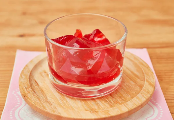 Organik çilek jelatin aperatifi küçük bir cam bardakta servis edilir ve pembe bir peçetenin üzerine bambu tabağı konur.
