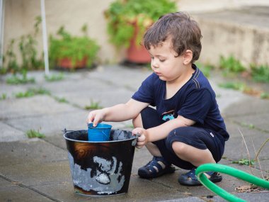 Delikanlı arka bahçede hortum ve kovalarla oynuyor.